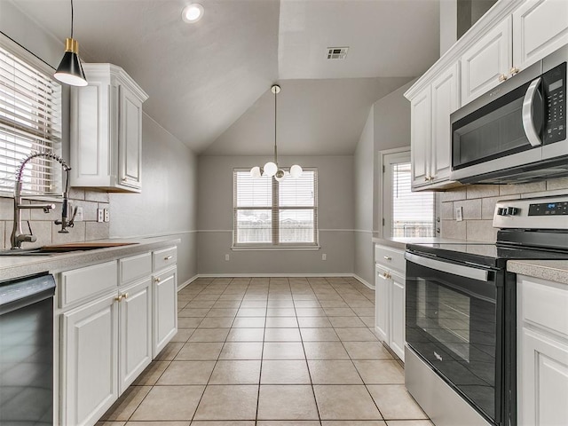 kitchen with appliances with stainless steel finishes, a sink, light countertops, vaulted ceiling, and decorative backsplash