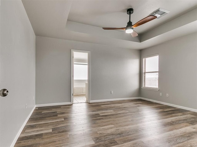 empty room featuring a raised ceiling, ceiling fan, wood finished floors, and baseboards