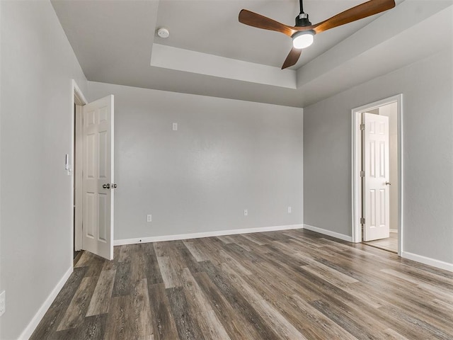 unfurnished room featuring a tray ceiling, wood finished floors, baseboards, ceiling fan, and a smoke detector
