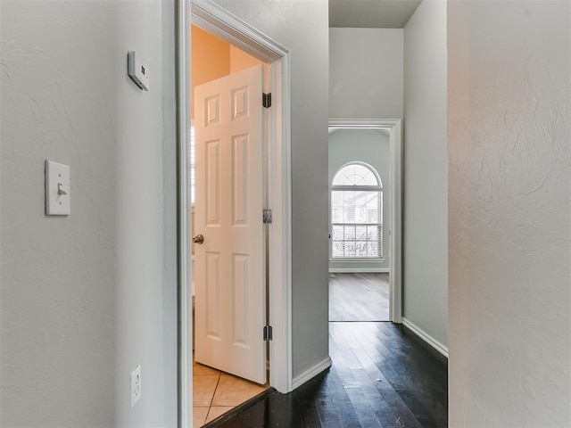 hallway with a textured wall, baseboards, and wood finished floors