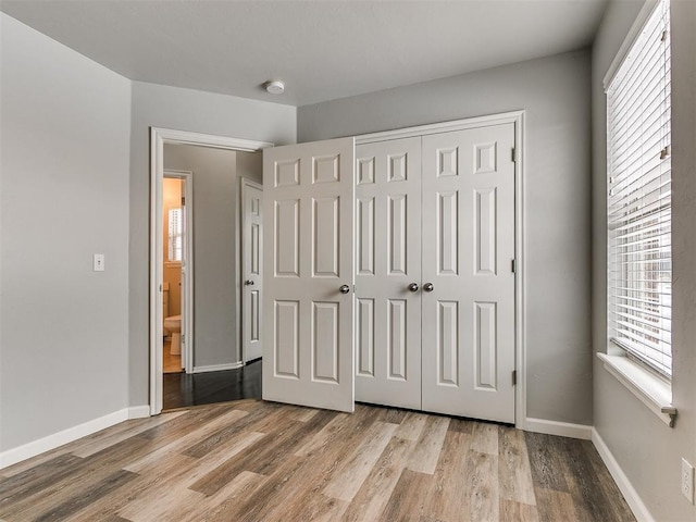 unfurnished bedroom featuring wood finished floors, multiple windows, and a closet