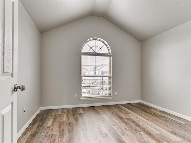 spare room featuring plenty of natural light, wood finished floors, lofted ceiling, and baseboards