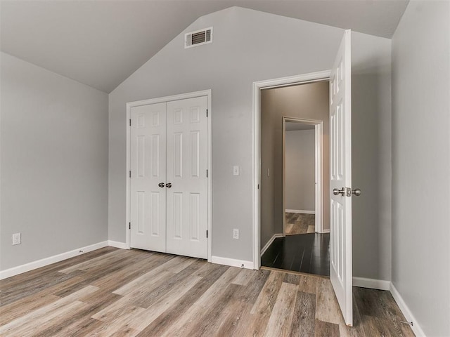 unfurnished bedroom featuring lofted ceiling, a closet, wood finished floors, and baseboards