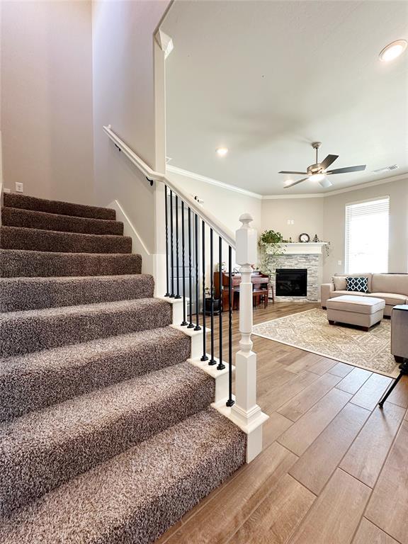 staircase featuring a ceiling fan, wood finished floors, a stone fireplace, ornamental molding, and recessed lighting
