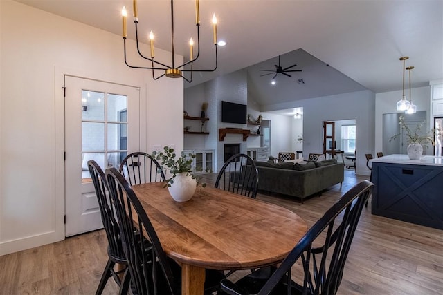 dining area featuring high vaulted ceiling, light wood-style flooring, a ceiling fan, a chandelier, and a fireplace