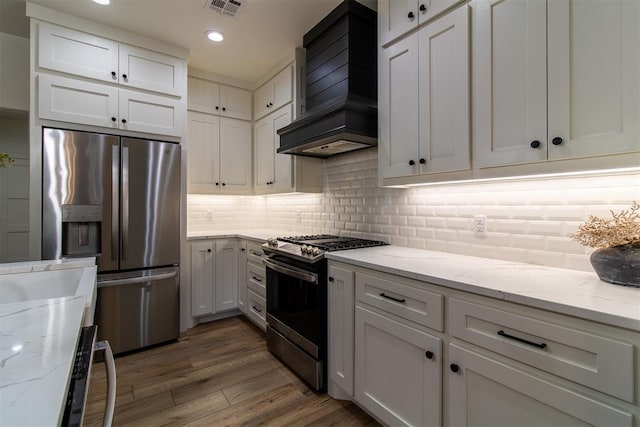 kitchen with appliances with stainless steel finishes, premium range hood, dark wood-style flooring, tasteful backsplash, and white cabinets