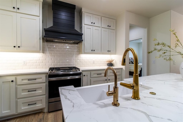 kitchen featuring wall chimney range hood, range with gas stovetop, tasteful backsplash, and light stone countertops