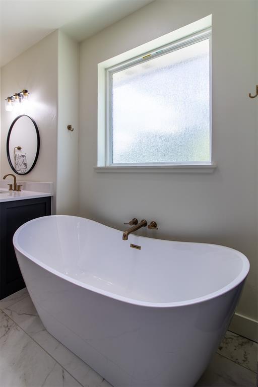 bathroom featuring vanity, plenty of natural light, marble look tile flooring, and a freestanding tub
