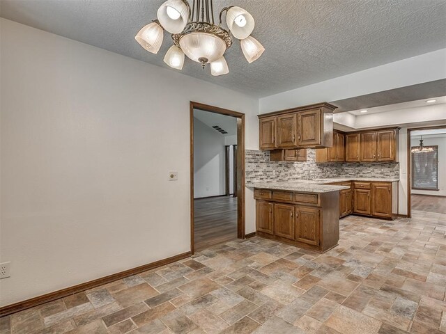 4400 Windsong Way, Oklahoma City, OK 73120 - kitchen with a chandelier, baseboards, brown cabinetry, light stone finish flooring, and decorative backsplash