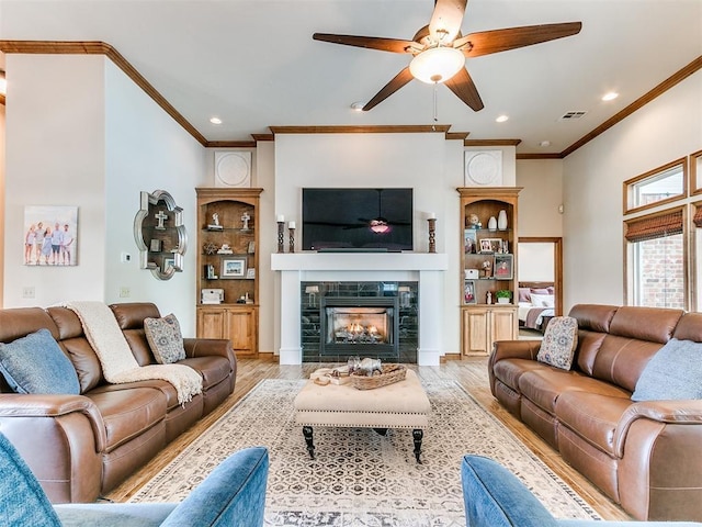 living area with crown molding, ceiling fan, wood finished floors, a tile fireplace, and recessed lighting