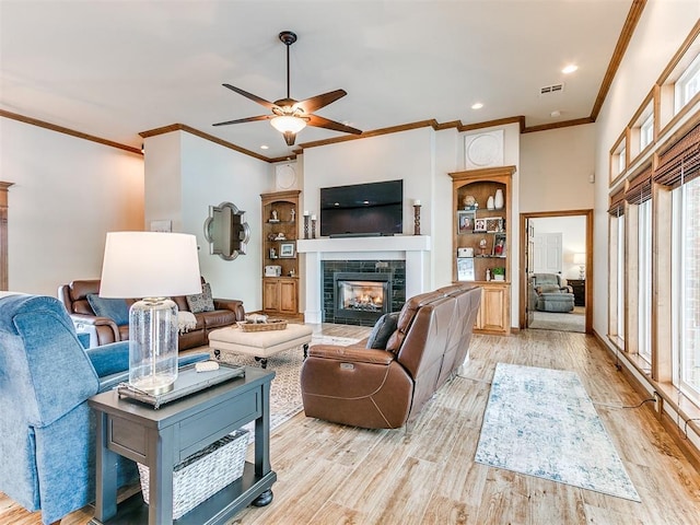 living room featuring crown molding, a tiled fireplace, a ceiling fan, light wood-style floors, and recessed lighting