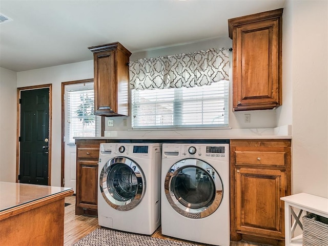 washroom featuring washing machine and dryer, cabinet space, and light wood-style floors