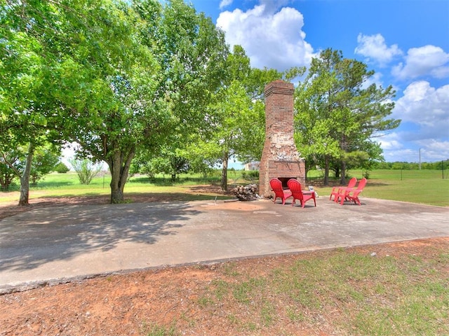 view of grassy yard with an outdoor stone fireplace and a patio