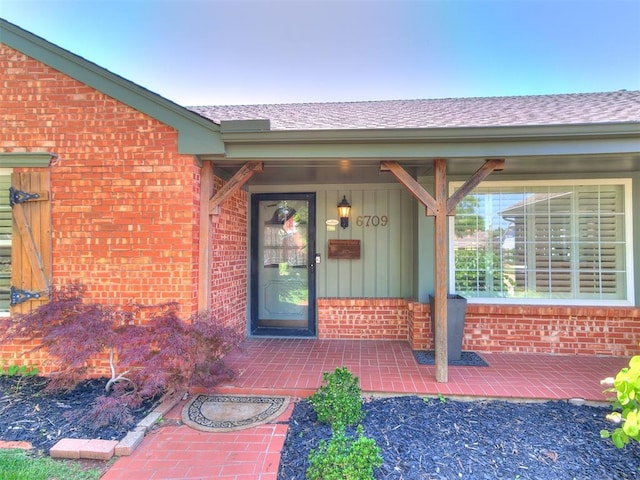 6709 Reed Dr, Oklahoma City, OK 73116 - view of exterior entry with brick siding, board and batten siding, a porch, and a shingled roof