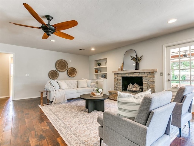 6709 Reed Dr, Oklahoma City, OK 73116 - living room featuring dark wood-type flooring, a ceiling fan, built in shelves, baseboards, and a stone fireplace