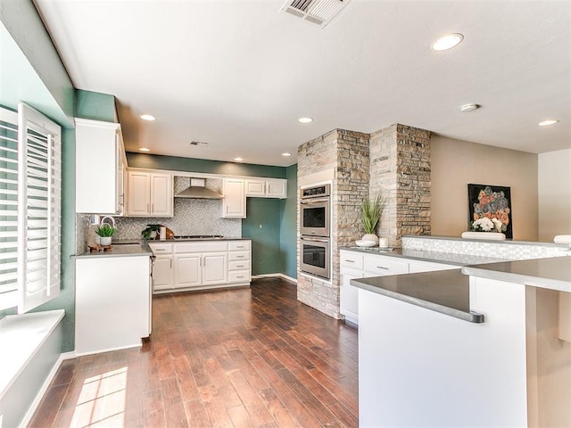 6709 Reed Dr, Oklahoma City, OK 73116 - kitchen featuring stainless steel double oven, wall chimney exhaust hood, dark wood-type flooring, white cabinetry, and decorative backsplash