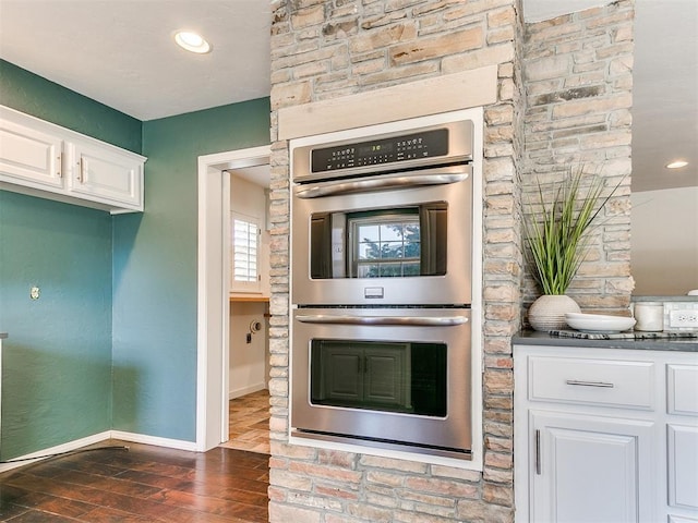 6709 Reed Dr, Oklahoma City, OK 73116 - kitchen featuring stainless steel double oven, dark wood-style flooring, white cabinets, baseboards, and dark countertops