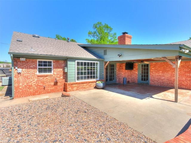 6709 Reed Dr, Oklahoma City, OK 73116 - back of property featuring brick siding, central AC unit, a chimney, a patio, and a shingled roof