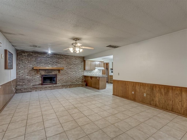 2915 N W Oaks Pl, Newcastle, OK 73065 - unfurnished living room featuring wood walls, a ceiling fan, a brick fireplace, a wainscoted wall, and a textured ceiling