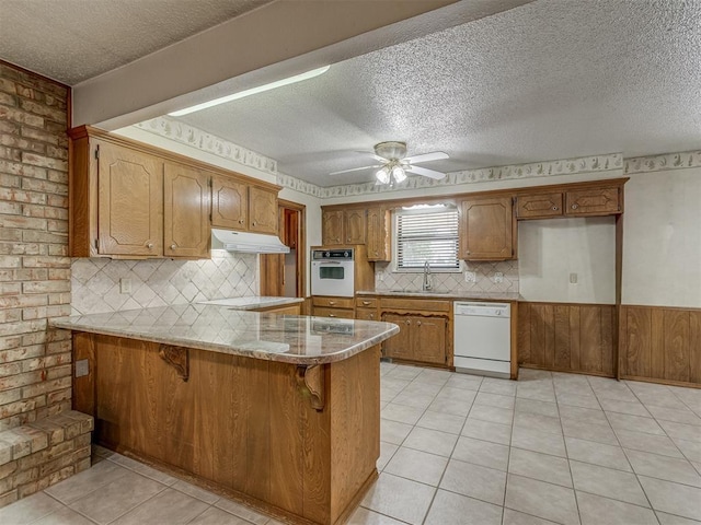 2915 N W Oaks Pl, Newcastle, OK 73065 - kitchen with white appliances, under cabinet range hood, a textured ceiling, a peninsula, and brown cabinetry