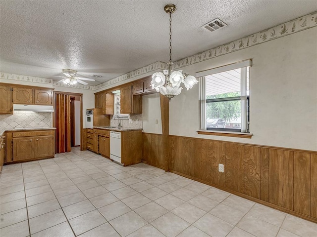 2915 N W Oaks Pl, Newcastle, OK 73065 - kitchen featuring dishwasher, a textured ceiling, brown cabinetry, a wainscoted wall, and a chandelier