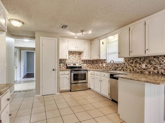 kitchen with stainless steel appliances, a sink, light tile patterned floors, backsplash, and white cabinets
