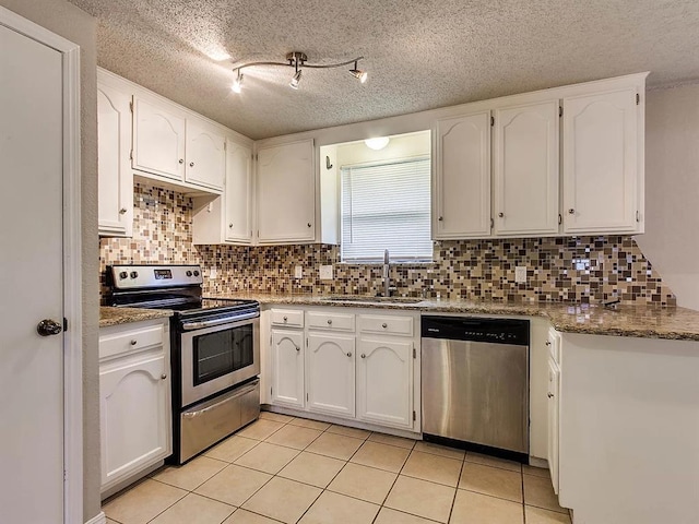 kitchen featuring appliances with stainless steel finishes, a sink, white cabinetry, light tile patterned flooring, and decorative backsplash