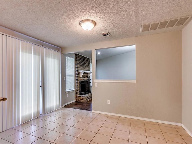 spare room featuring a textured ceiling, baseboards, a fireplace, and light tile patterned flooring