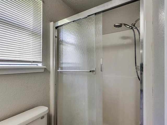 full bathroom featuring toilet, a shower stall, and a textured wall