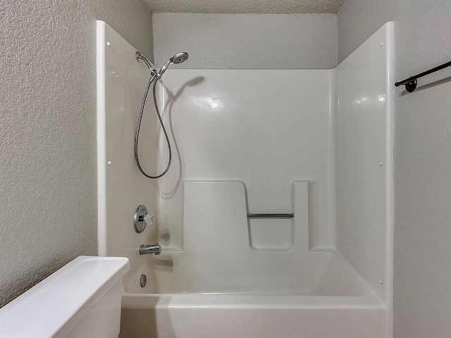 full bathroom featuring a textured wall, washtub / shower combination, and toilet