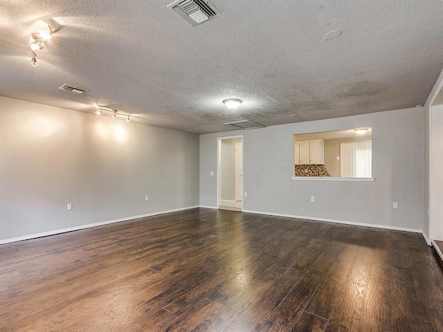 empty room featuring dark wood finished floors, a textured ceiling, track lighting, and baseboards