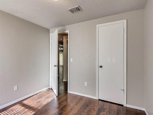 unfurnished bedroom featuring wood finished floors, a textured ceiling, baseboards, and a textured wall
