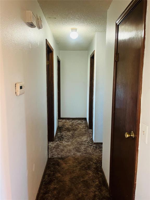 2217 7th St, Prague, OK 74864 - corridor featuring dark colored carpet and a textured ceiling