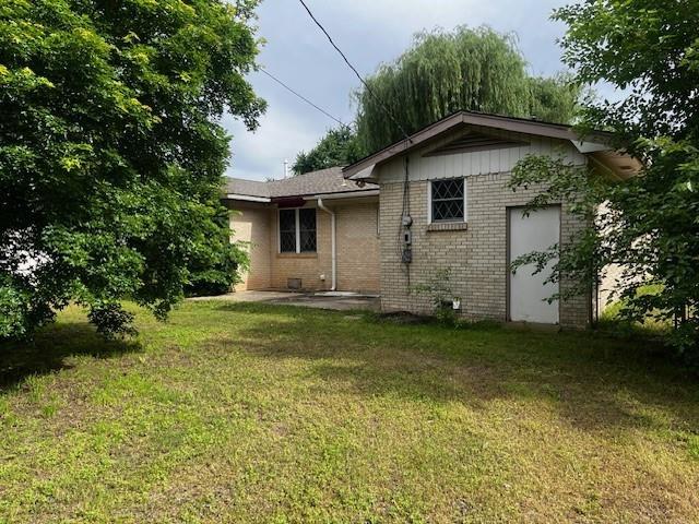 306 W Comanche St, Lindsay, OK 73052 - rear view of house featuring brick siding, a lawn, and a patio area
