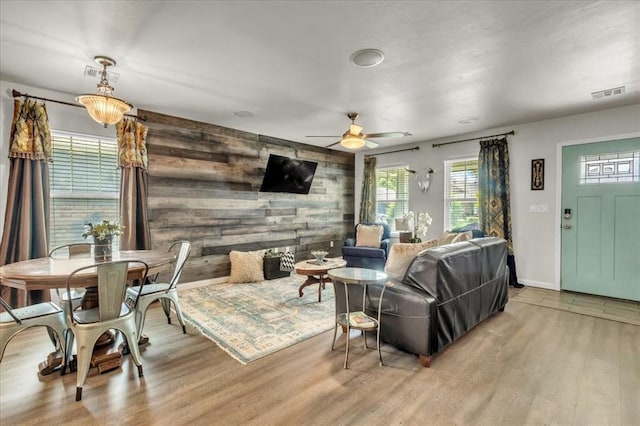 living room with wooden walls, plenty of natural light, light wood-type flooring, ceiling fan, and baseboards