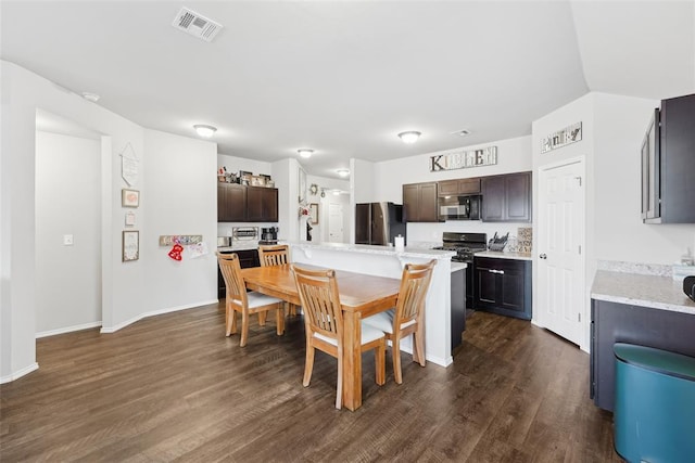 kitchen featuring freestanding refrigerator, black microwave, light countertops, a breakfast bar, and dark wood-type flooring