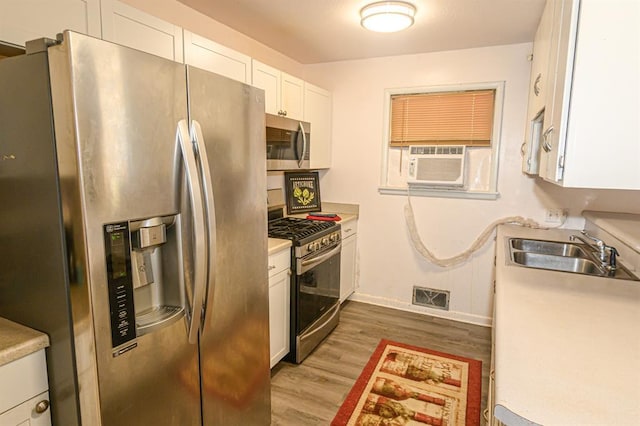 kitchen with appliances with stainless steel finishes, a sink, white cabinetry, light wood-style floors, and light countertops
