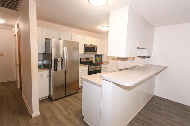 kitchen featuring appliances with stainless steel finishes, dark wood-style flooring, white cabinetry, a peninsula, and a sink