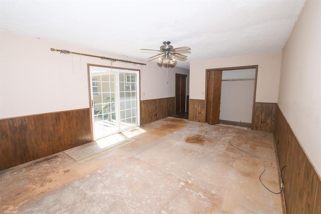 empty room featuring wainscoting, wood walls, and a ceiling fan
