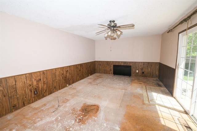 empty room featuring a wainscoted wall, wood walls, and a ceiling fan