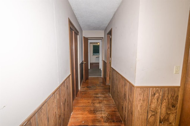 corridor featuring a textured ceiling and a wainscoted wall