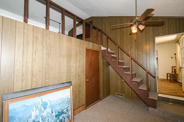 stairway with wood walls, ceiling fan, vaulted ceiling, and carpet flooring
