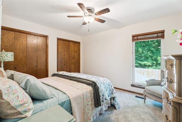 bedroom with light colored carpet, multiple closets, baseboards, and a ceiling fan