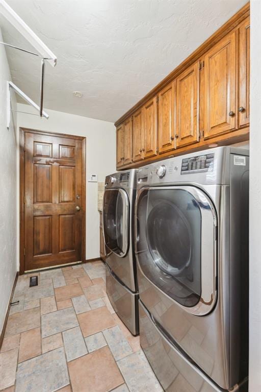 clothes washing area with washer and clothes dryer, cabinet space, baseboards, and stone finish floors