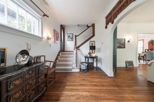 foyer featuring arched walkways, stairway, wood finished floors, crown molding, and baseboards