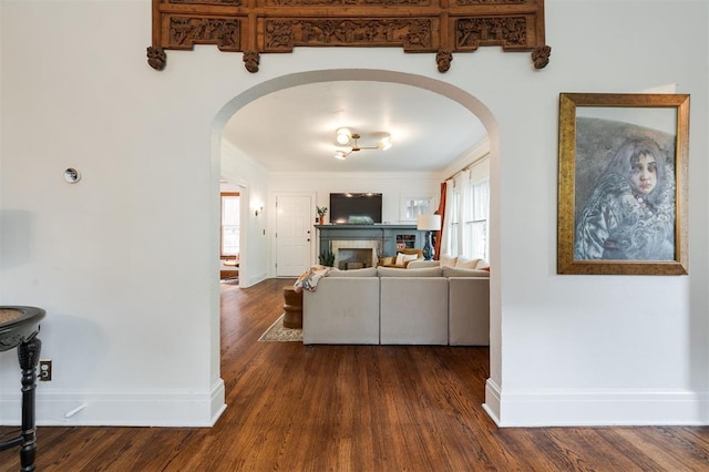 living area with arched walkways, dark wood-type flooring, and baseboards