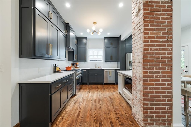 kitchen featuring appliances with stainless steel finishes, light wood-style floors, a chandelier, a sink, and light countertops