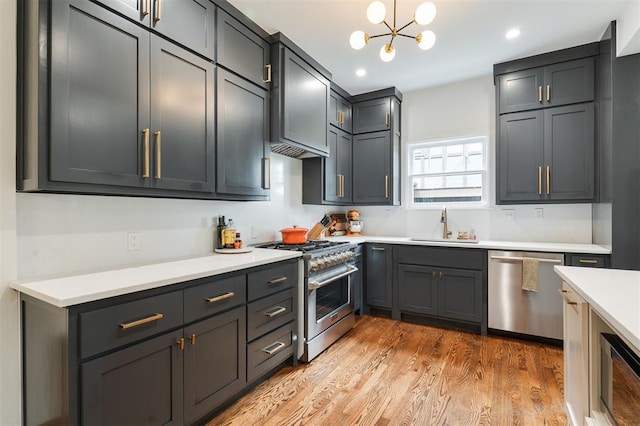 kitchen with appliances with stainless steel finishes, a sink, light countertops, light wood finished floors, and a chandelier