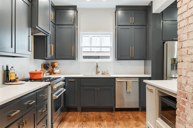 kitchen with appliances with stainless steel finishes, a sink, wood finished floors, and light countertops