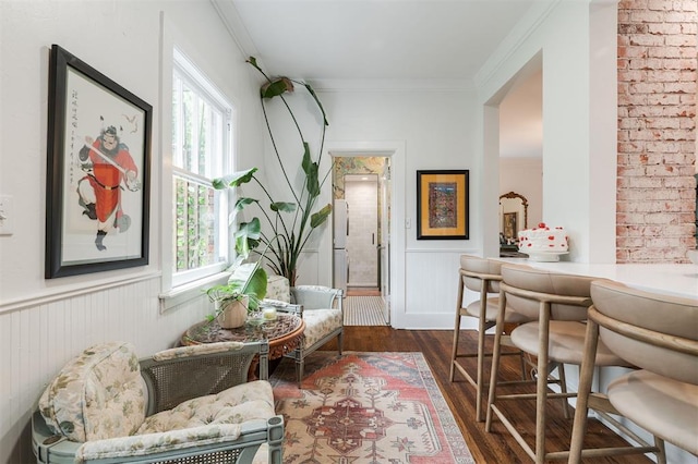 sitting room with dark wood-style floors, ornamental molding, and wainscoting